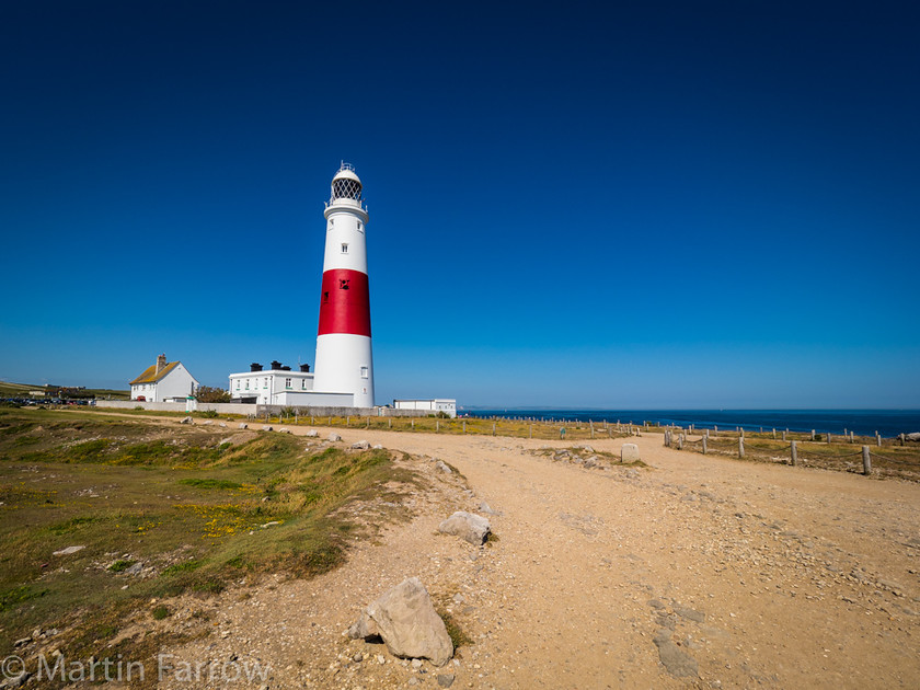 Portland-Lighthouse 
 Portland lighthouse against clear blue sky 
 Keywords: Dorset, Portland, blue sky, landscape, light, lighthouse, navigation, red stripe, safety, sea, summer, sun, tower, view