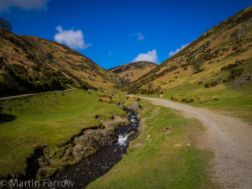 Into-The-Hills 
 View up a valley with footpath and stream between hills 
 Keywords: Long Mynd, Shropshire, blue, clouds, curve, green, hills, landscape, path, spring, stream, valley, walking