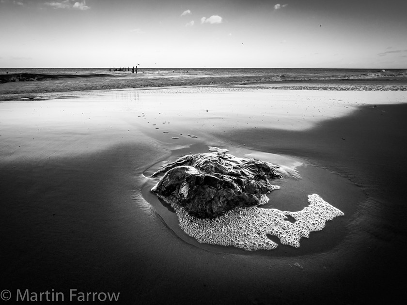 Falling-Tide 
 Single rock on sandy beach with tide receding leaving wet sand, monochrome 
 Keywords: Happisburgh, Norfolk, coast, defences, foam, lone, monochrome, pool, rock, sand, sea, shore, simple, timbers, waves, wet, winter